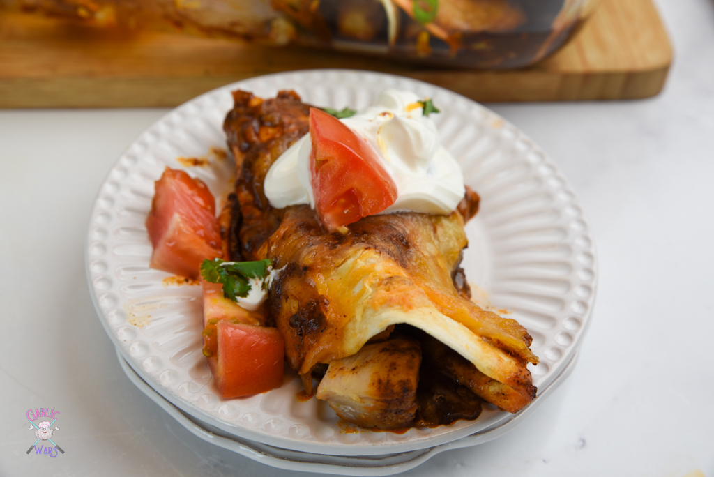 chicken enchilada on small white plate, topped with sour cream and tomatoes