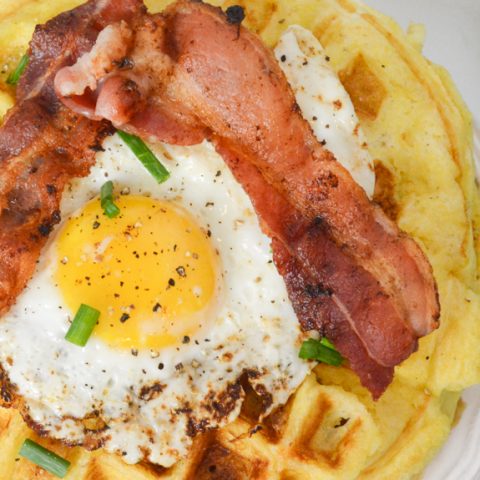 fried egg on top of a waffle with strips of bacon