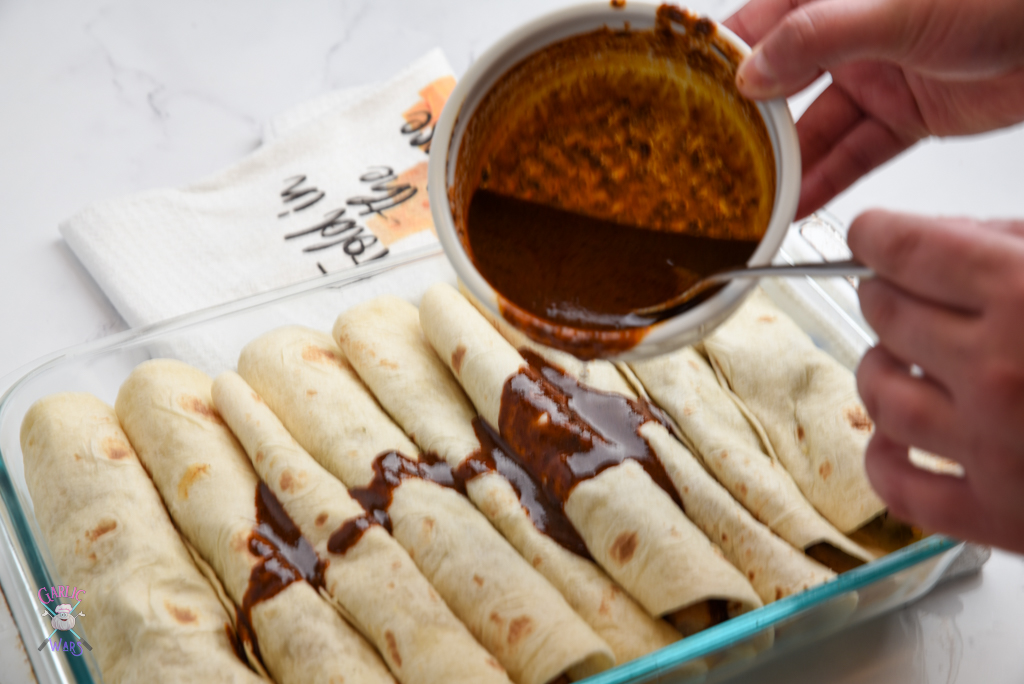 pouring enchilada sauce over the tortillas