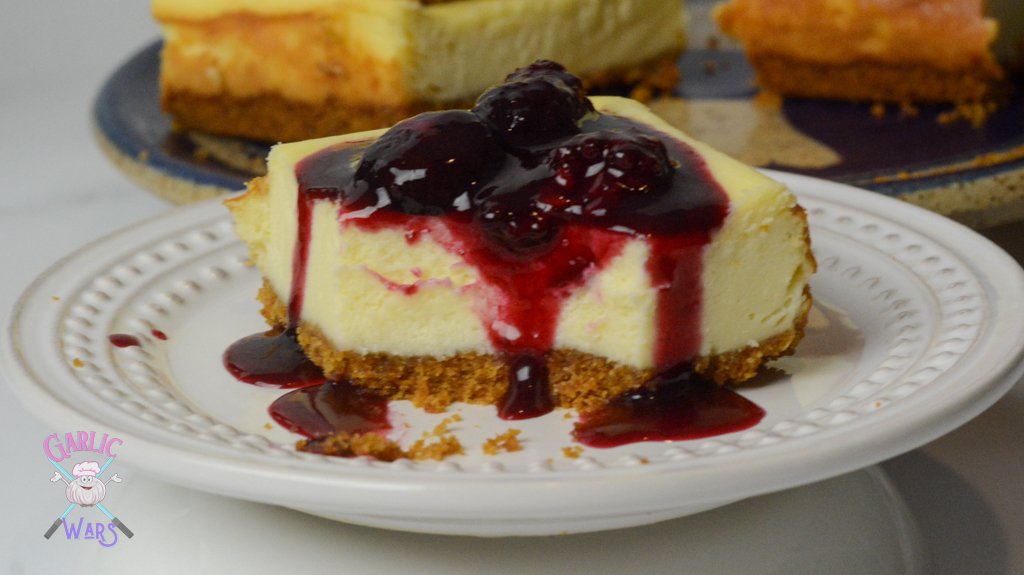 cheesecake bar on small white plate, topped with red wine sauce and whole berries