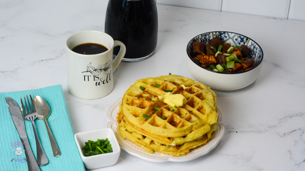 A place setting with a cup of coffee, a bowl of sweet potato home fries, and a plate of waffles. 