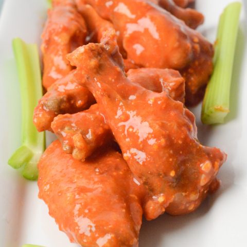 air fryer chicken wings tossed in buffalo sauce on a white plate with celery