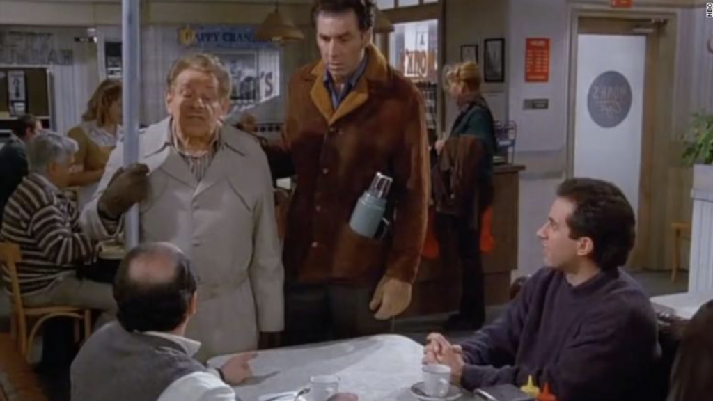 George and Jerry in Monk's coffee shop, with Frank holding an aluminum pole and Kramer standing beside him.