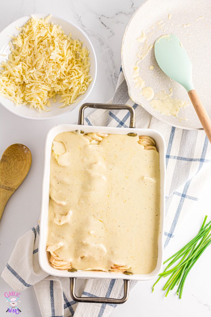 swiss and parmesan cheese sauce poured over potatoes in a casserole pan