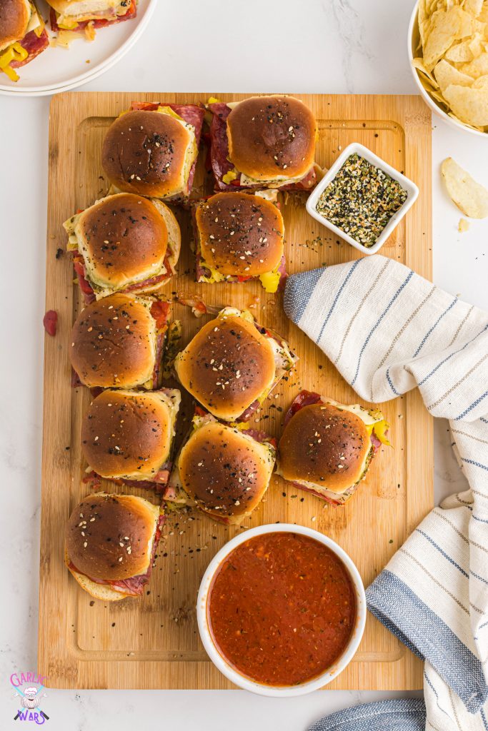 italian sliders arranged on serving board with marinara sauce and a blue striped tea towel