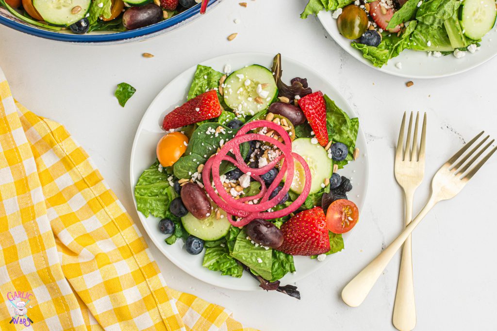 summer salad with pickled red onions on a small white plate with a yellow checkered cloth