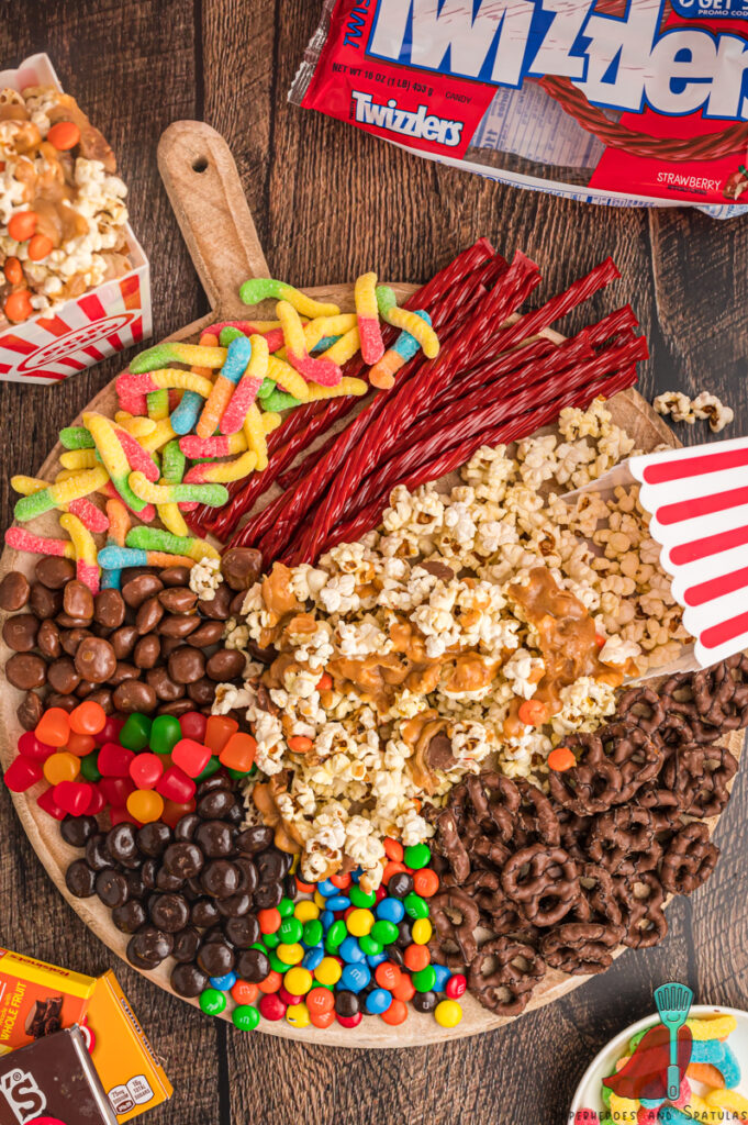 candy, popcorn, and pretzels arranged on a large circular cutting board
