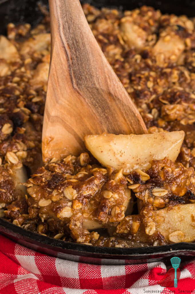 wooden spoon holding up pear cobbler in pan